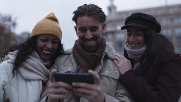 Three Diverse Friends Using Mobile Phone While Standing Outdoors in City Street
