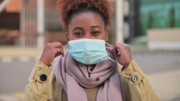 Young attractive black woman taking off medical mask and smiling in relief