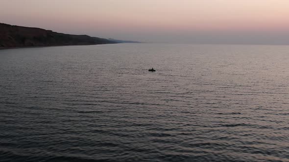 Drone flying around lonely boat at sunrise.