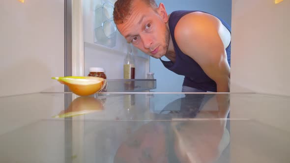 man looks into refrigerator, looks at onion and takes a bottle of alcohol.