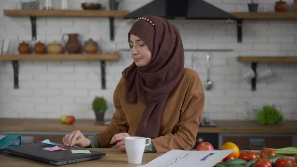 Young Female Middle Eastern Startuper Closing Laptop and Thinking Sitting in Kitchen