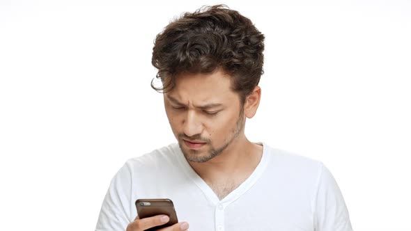 Displeased Young Handsome Man Looking at Phone Over White Background