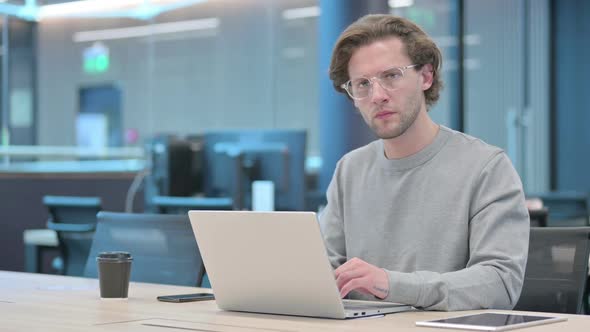 Young Businessman Looking at Camera While Using Laptop in Office