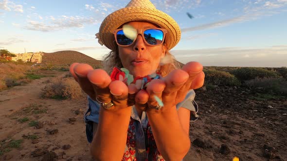 Woman with sunglasses and hat blowing confetti from her hands