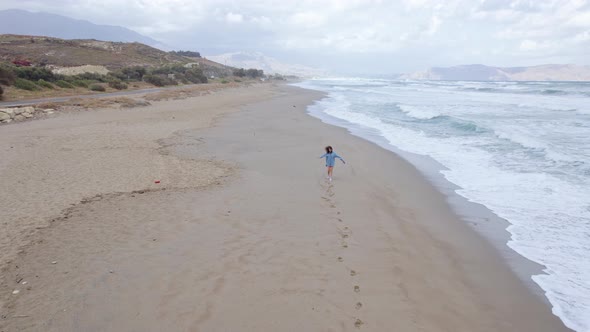 Drone footage of a woman running along the ocean coastline and leaving footprints in the sand.