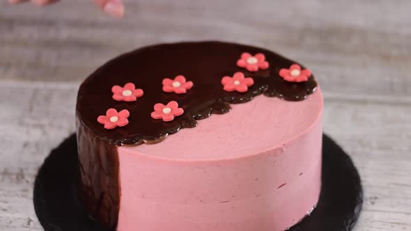 Female Hands Decorate Homemade Strawberry Mousse Cake with Sugar Flowers.