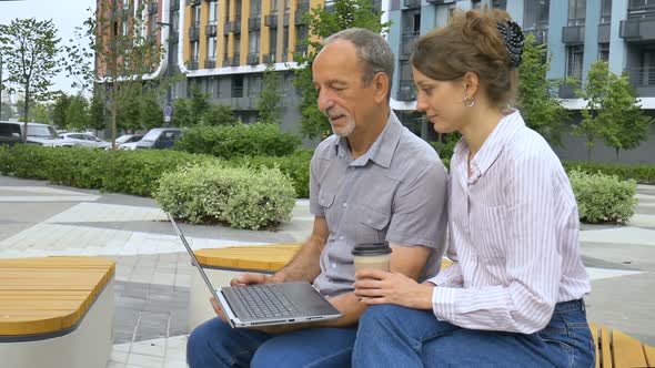 Young Employee is Teaching Her Older Colleague How to Use Laptop and Corporate Software Sitting on
