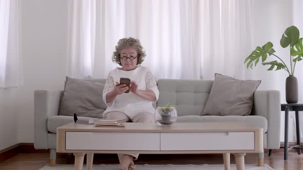 Asian woman elderly play smart phone on sofa in living room with relaxing day.