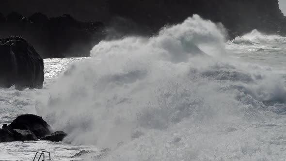 Giant Wave Rolls To Rocky Shore. Spray From Crashing Waves Flys Over the Spurs. Slow Motion Shot.