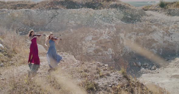 Female Duet of Violinists in Blowing Dresses Play Music Among Cliffs