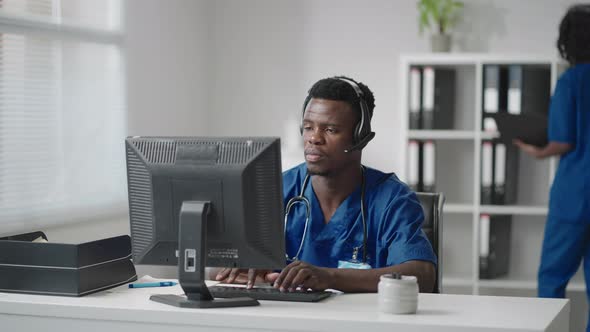 Afroamerican Male Doctor or Nurse with Headset and Computer Working at Hospital 