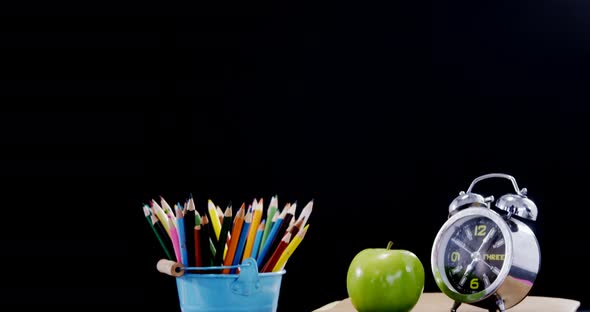 Apple and alarm clock on book stack with school supplies