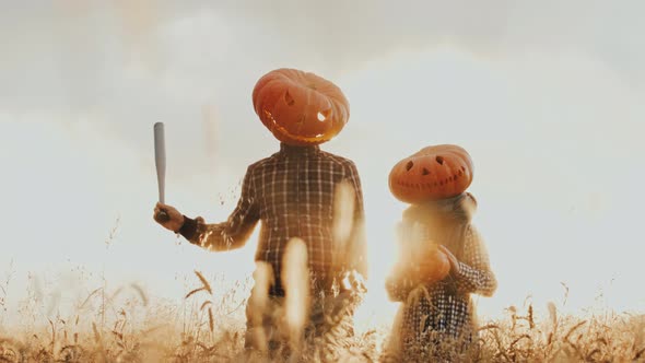 Funny People in Giant Pumpkin Heads Fool Around at the Camera in the Middle of the Field