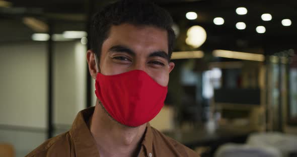 Portrait of a mixed race businessman wearing face mask looking at camera in modern office