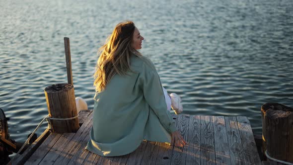 Blonde Girl Sitting on a Wooden Pier Back View