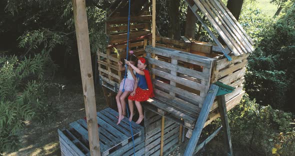 Girls wearing superhero disguises, sitting on treehouse