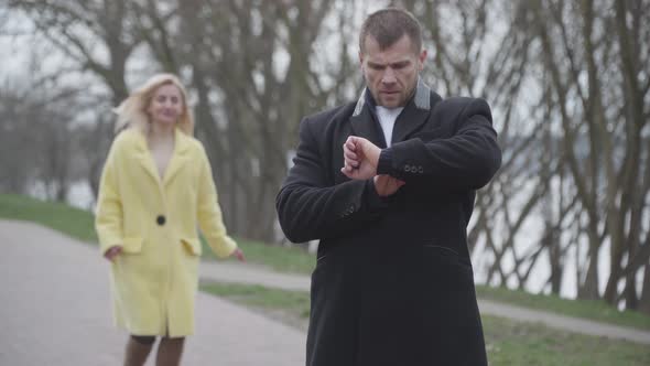 Smiling Blond Caucasian Woman Approaching Elegant Man Waiting for Her and Closing His Eyes