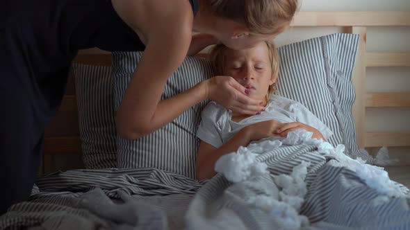 A Sick Little Boy in a Bed Mother Kisses Him and Measures His Temperature Baby Flu Concept