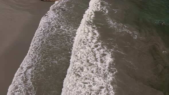 aerial view of foaming waves of the pacific ocean hitting the sandy beach