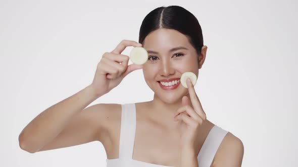 Cute female model clean fresh skin is holding sliced of cucumber. Expressive facial expressions.