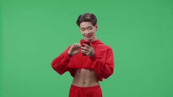 Happy Young Asian Transgender Male Use Mobile Phone While Standing On Green Screen In The Studio