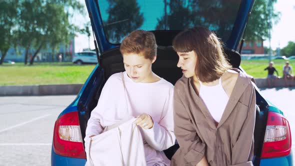 Two Girls in the Parking Lot at the Open Trunk