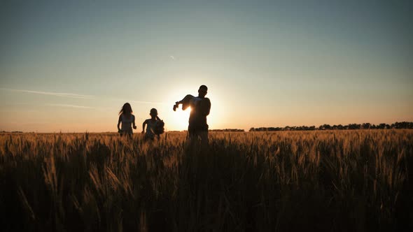 Happy Family Walking in Wheat Field on Sunset in a Warm Summer Evening. Little Son Sitting on Her