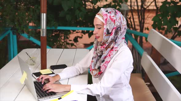 A Modern Muslim Woman in a Hijab Prints a Letter To a Business Partner on Laptop