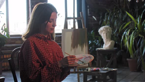 A Young Woman Artist Mixing Colors on a Wooden Palette  Looking in the Camera