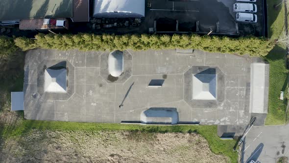 Descending top down aerial view of a lone skater at an urban skateboard park.