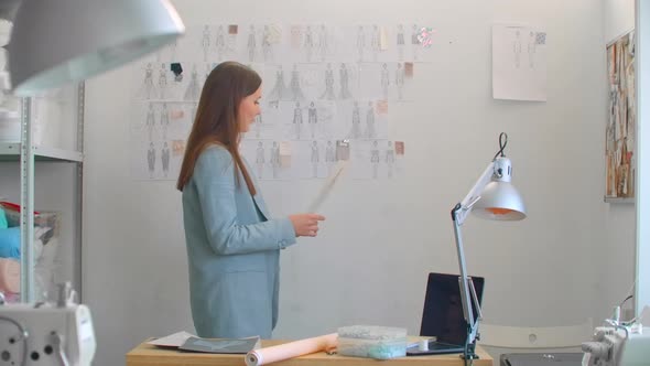 Young Fashion Designer Standing with Back to Camera Looking at Drawings Sketches Hanging on Wall