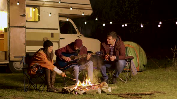 Man Singing a Song on Guitar for His Friends Around Camp Fire