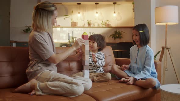 Young Asian Mother and Little Siblings Spend Time at Modern Flat Play Together Seated on Sofa Enjoy