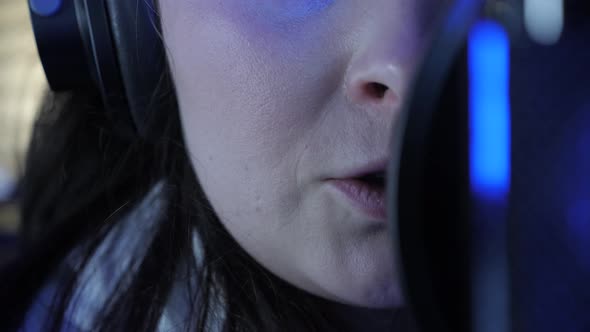 Young professional female singer in headphones singing in recording studio