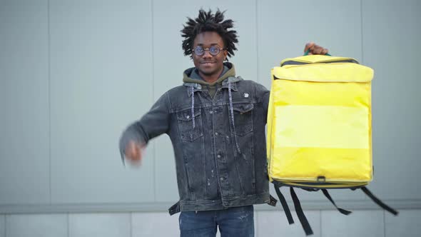 Cheerful African American Young Man Showing Thumb Up Raising Yellow Insulated Food Delivery Bag