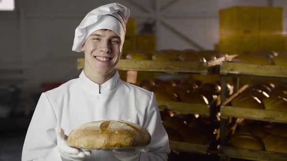 Happy Baker Holds a Fresh Loaf of Bread in a Hand and Shows a Thumb at Camera