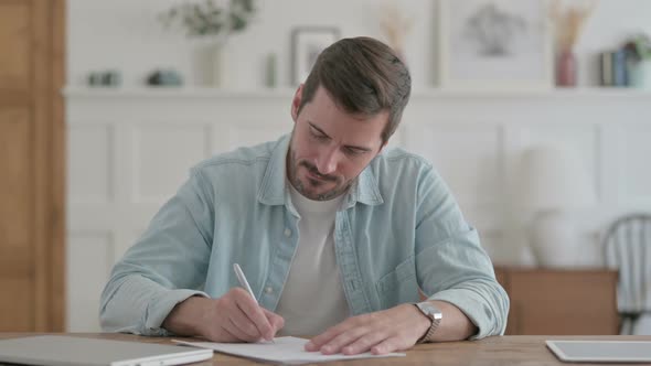 Tense Young Man Trying to Write on Paper in Office