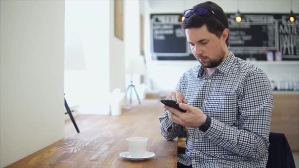 An Adult Man Communicates on the Phone Sitting in a Coffee House