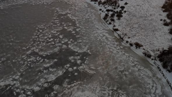 Landscape with frozen lake and mountains in background at sunset. Aerial tilt-up reveal