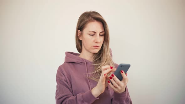 Pleased Blond Woman in Hoodie Using Her Smartphone and Looking To the Camera