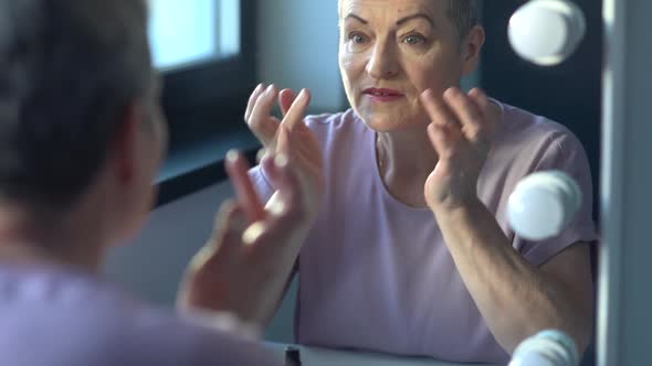 A Mature Woman in a Pink Dressing Gown Looks in the Mirror