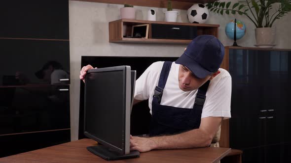 Closeup of a Male Handyman in Overalls Repairs a Computer Monitor