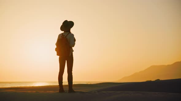 Young hiker with a backpack looking at the mountains at sunset