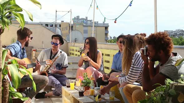 Two guys playing guitar and saxophone, friends listening and swaying to the beat