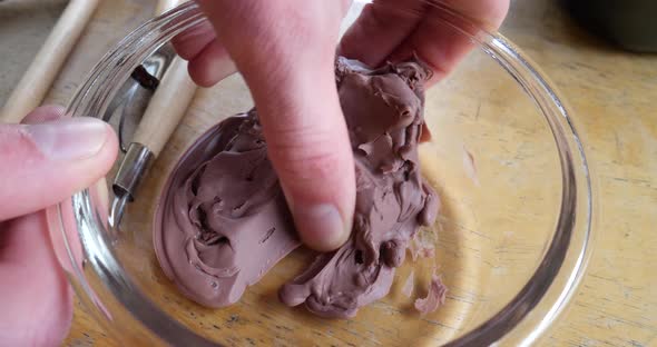 An artist squishing and shaping very soft, brown modeling clay in a glass dish during a sculpting pr