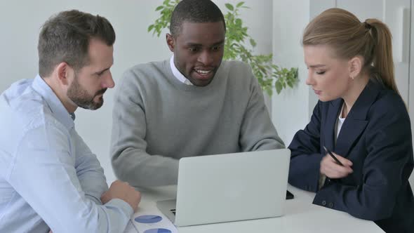 Male and Female Business People Discussing While Using Laptop in Office