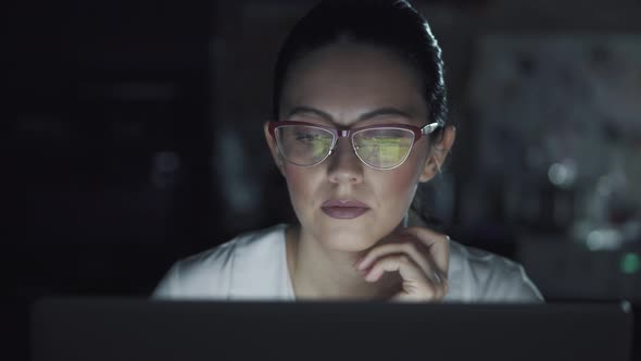 Woman in Glasses Works on a Laptop in the Dark. Portrait of a Girl Spending Time at the Computer