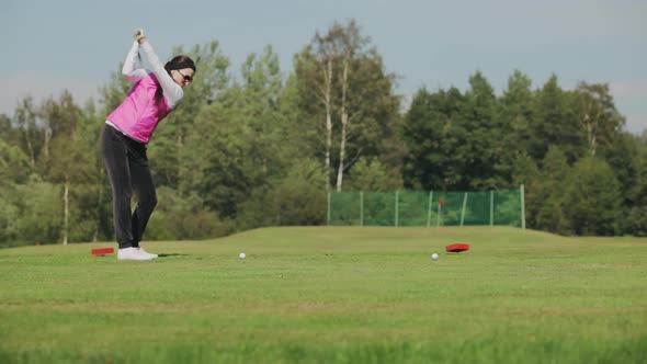 Girl in Sunglasses and a Pink Vest Hits a Ball with a Club While Playing Golf on a Green Golf