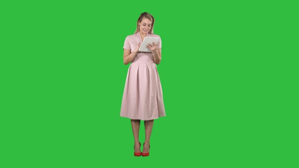 Pretty young woman in pink dress holding tablet and looking