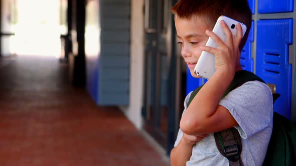 Happy schoolboy talking on mobile phone in corridor 4k